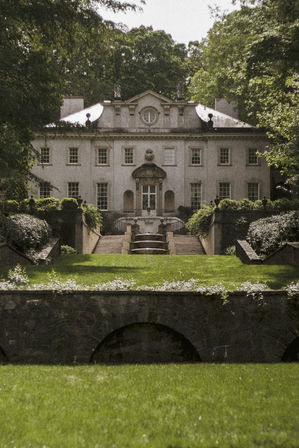 Manoir historique en pierre avec jardins paysagers et fontaine centrale.